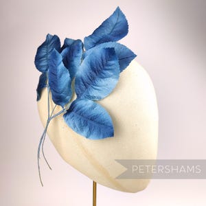 Könnte beinhalten: Ein blauer Blatt-Haarkamm auf weißem Hintergrund. Der Kamm ist aus Stoff und hat ein zartes, weibliches Design. Petershams.