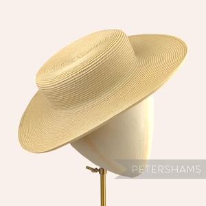 May include: A wide-brimmed straw hat with a flat crown. The hat is a light beige color and has a woven texture.