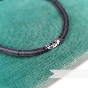 May include: A close-up of a black sequin trim, made of small, round sequins, arranged in a circle. The sequins are sewn together with a silver thread. The trim is lying on a green velvet fabric.