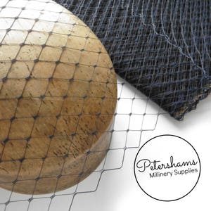 Può includere: Un primo piano di un tessuto a rete nero con un motivo a rombi. La rete è drappeggiata su una forma di cappello in legno. Il testo "Petershams Millinery Supplies" è visibile nell'angolo in basso a destra dell'immagine.