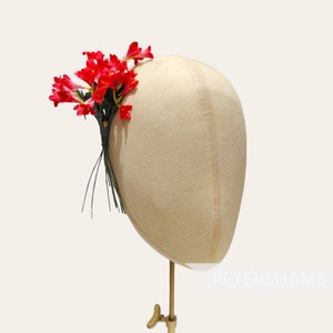 May include: A mannequin head with a red flower crown made of artificial flowers. The crown is made of red flowers with green leaves.