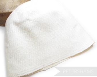 May include: A white, textured beanie hat. The hat is made of a woven fabric and has a rounded crown. The hat is a solid off-white color and is displayed on a white background. The word "PETERSHAMS" is in the bottom right corner.