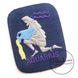 May include: An embroidered iron-on patch featuring the astrological sign Aquarius. The patch is navy blue with a silver embroidered figure pouring water from a pitcher. The word "Aquarius" is embroidered in purple below the figure.