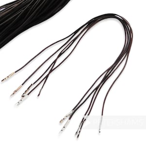 Könnte beinhalten: Ein Bündel aus zehn braunen Lederbändern mit silbernen Metallspitzen. Die Bänder sind etwa 30 cm lang.