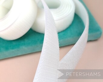 May include: White hook and loop tape, also known as Velcro, is rolled up on a teal surface. The tape is soft and fuzzy, and it is perfect for attaching fabrics together.
