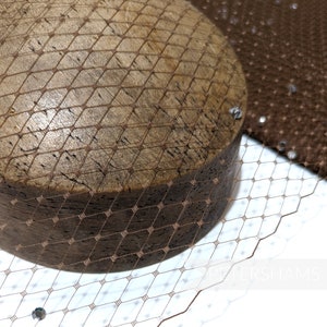 May include: A close-up of a brown hat with a brown netting. The hat is on a wooden form. The netting is a fine mesh with a diamond pattern.