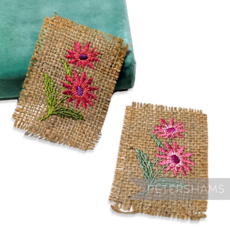 Pode incluir: Duas bases de juta com flores rosa bordadas e folhas verdes. As flores t&ecirc;m centros roxos. As bases t&ecirc;m uma borda desfiada.