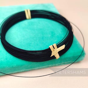 May include: A black wire choker necklace with a gold accent. The necklace is on a turquoise velvet background.