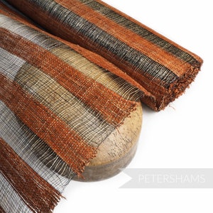 Könnte beinhalten: Nahaufnahme einer Rolle orange-schwarzes, gestreiftes Mesh-Band. Das Band ist mit einem Metallic-Faden gewebt und hat einen ausgefransten Rand.