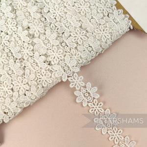 May include: White crocheted lace trim featuring a delicate floral design. The trim is approximately 1 inch wide and is ideal for adding a touch of elegance to any project.