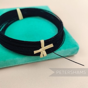 May include: A black cord bracelet with a natural wood accent. The bracelet is on a turquoise blue velvet surface.