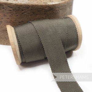 May include: A spool of olive green grosgrain ribbon. The ribbon is on a wooden spool and is approximately 2.5 cm wide.