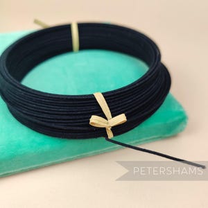 Könnte beinhalten: Eine Spule schwarzes Petersham-Band, um ein tealblaues Samtkissen gewickelt. Das Band ist mit einer naturfarbenen Schleife gebunden.