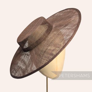 Op de afbeelding: Een bruine zonnehoed met een brede rand en een kleinere, cilindrische kroon. De hoed is gemaakt van een geweven materiaal en wordt getoond op een paspop. De tekst "PETERSHAMS" is zichtbaar in de rechter benedenhoek.