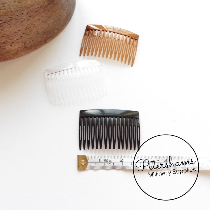 May include: Three plastic hair combs in different colors: brown, clear, and black. The combs are approximately 2 inches long and have a rectangular shape. The combs are arranged on a white surface with a measuring tape.