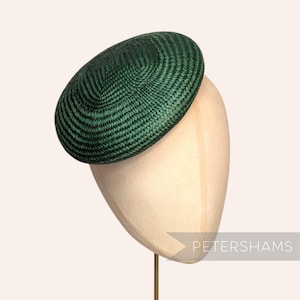 May include: A dark green woven hat with a circular design, displayed on a mannequin head. The hat is a deep forest green and has a textured appearance. The word "PETERSHAMS" is printed in white on the lower right side of the image.