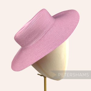 May include: A pink wide-brimmed straw hat with a slightly indented crown. The hat is on a white hat stand.