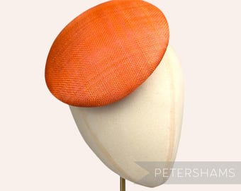 May include: A bright orange, round hat made of woven straw. The hat is perched on a white hat form.