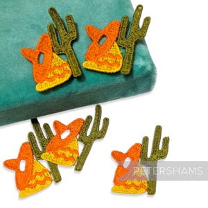 Peut inclure: Écussons brodés sur le thème du désert. Les écussons représentent des chapeaux de cowboy orange et jaunes et des cactus verts. Les écussons sont disposés sur une surface en velours vert sarcelle. Le mot "PETERSHAMS" est visible dans le coin inférieur droit.