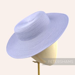 May include: A light blue wide-brimmed straw hat with a flat crown. The hat is on a display stand.