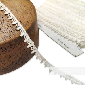 May include: White cotton lace trim with a scalloped edge. The trim is shown wrapped around a wooden spool and on a white card that reads "100 yds Yards".