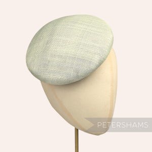 May include: A light green, woven fabric hat with a rounded crown, displayed on a mannequin head. The hat has a textured appearance and is set against a neutral background. The text "PETERSHAMS" is visible.