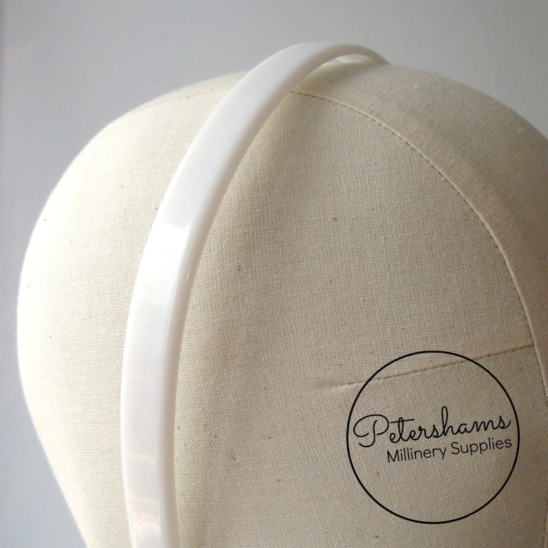 May include: White plastic headband for millinery. The headband is 1/2 inch wide and is shown on a millinery head block.