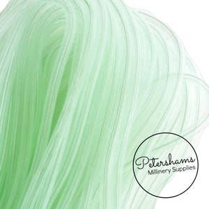 May include: A close-up of a light green, sheer, pleated ribbon. The ribbon is made of a soft, delicate material and has a subtle sheen. The ribbon is ideal for adding a touch of elegance to any project.