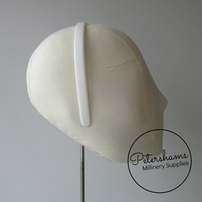 May include: White plastic headband for millinery, shown on a white millinery head form. Petershams Millinery Supplies.