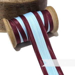 Op de afbeelding: Een spoel met blauw en donkerrood gestreept lint. Het lint is om een houten spoel gewikkeld.