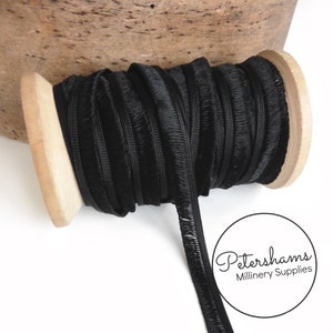 May include: A spool of black velvet trim with a fringed edge. The trim is wound around a wooden spool. The spool is labelled "Petershams Millinery Supplies".