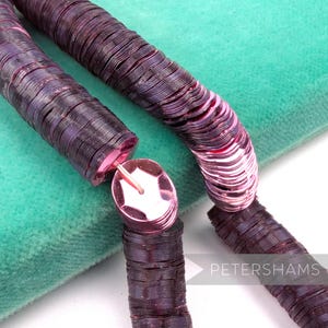 May include: Close-up of dark purple sequins on a spool, with a pink center. The sequins are arranged in a spiral pattern. The background is a soft, teal green fabric. The word "PETERSHAMS" is visible in the bottom right corner.