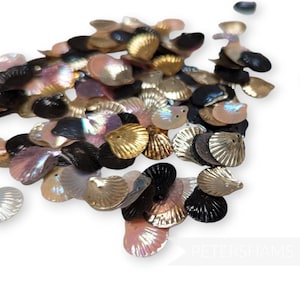 May include: A collection of iridescent seashell-shaped sequins in various colors, including gold, black, pink, and white. The sequins are scattered, creating a textured and decorative effect. The sequins are likely used for embellishment in crafts or fashion.