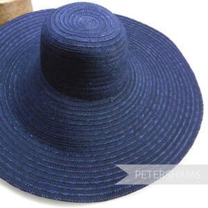 Peut inclure: Un chapeau de soleil à large bord de couleur bleu foncé avec un léger scintillement. Le chapeau est fait de paille tissée et a un bord large et plat.