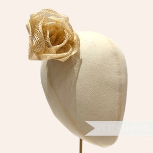 May include: A large, golden, woven flower hair accessory. The flower is made of a delicate, straw-like material and is arranged in a spiral shape.