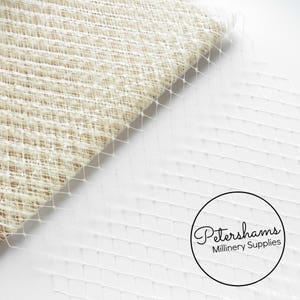 May include: White netting fabric with a diamond pattern. The fabric is folded in half, showing the texture of the netting. Petershams Millinery Supplies is printed on a white circle in the lower right corner.