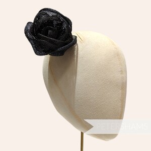 May include: A black mesh rose hair clip on a white mannequin head. The mannequin is on a gold stand. The text "PETERSHAMS" is visible on the mannequin's neck.