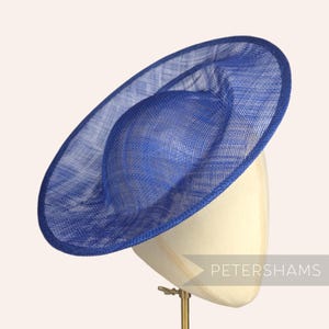 May include: A blue, wide-brimmed hat made of woven straw, sitting on a hat stand. The hat is slightly tilted to the side.