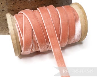 May include: A spool of peach-colored velvet ribbon wound around a wooden spool. The ribbon is approximately 1/2 inch wide.