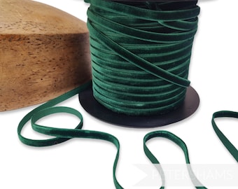 May include: A spool of dark green velvet ribbon. The ribbon is wound around a black spool and is lying on a wooden surface.