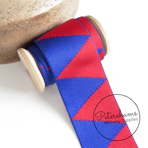Op de afbeelding: Rood en blauw geometrisch patroon lint op een houten spoel. Petershams Millinery Supplies.