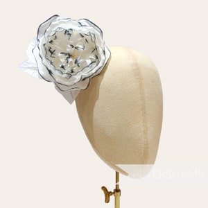 May include: A white and black fabric flower with a layered design, displayed on a mannequin head.