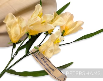 May include: A cluster of pale yellow artificial flowers with green stems and leaves. The flowers have a delicate, textured appearance. A tag reads "No. 784 pale apricot 8420 Made in German Democratic Republic". The word "PETERSHAMS" is also visible.