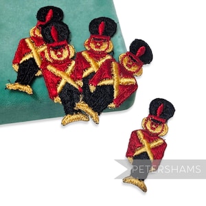Könnte beinhalten: Gestickte Aufnäher mit Spielzeugsoldaten-Designs. Die Aufnäher haben rote Jacken, schwarze Hosen und schwarze Hüte mit goldenen Akzenten. Die Aufnäher sind in verschiedenen Größen und befinden sich auf einer grünen Oberfläche. Der Text "PETERSHAMS" ist sichtbar.
