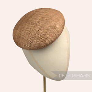 May include: A brown straw hat with a round, flat crown. The hat is displayed on a white hat stand.