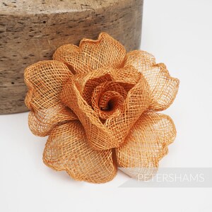May include: A large, brown, woven rose flower made of burlap fabric. The rose is a single bloom with a center that is curled inward.