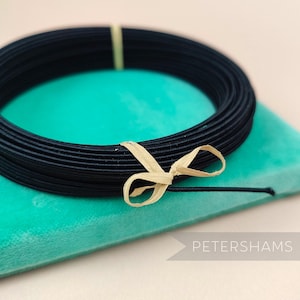 May include: A spool of black Petersham ribbon tied with a beige ribbon. The ribbon is on a turquoise surface.