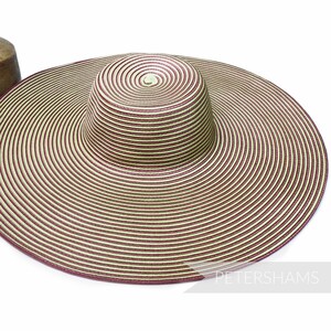 May include: A wide-brimmed sun hat with a spiral design. The hat features alternating stripes of cream and burgundy. The crown is cylindrical, and the brim is wide and circular. The hat is designed to provide shade from the sun.