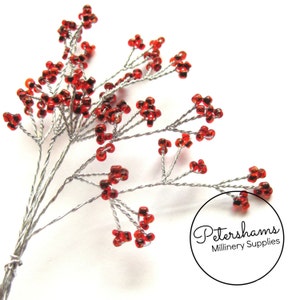 以下が含まれることがあります： 銀色のワイヤーの茎に赤いビーズでできた花のスプレー。スプレーは、ベリーのような小さなビーズが密集して作られています。Petershams Millinery Supplies.