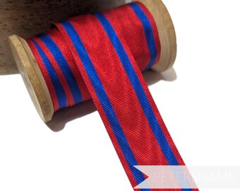 May include: Red and blue striped ribbon wound around a wooden spool. The ribbon is a classic striped pattern with two blue stripes on a red background.